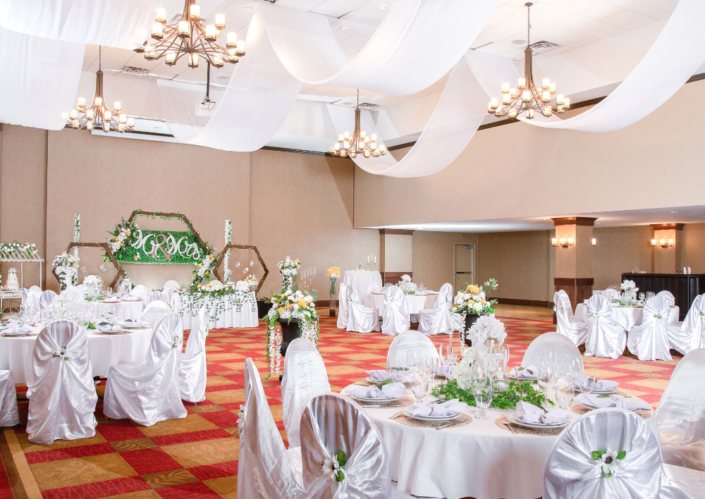 Banquet tables set with flowers, wine glasses, and napkins in an upscale room for events. The Ralph Pomeroy Ballroom at the Pomeroy Hotel & Conference Centre - Fort St. John in Alberta, Canada can be used to host upscale events, weddings, banquets, corporate events, and more.